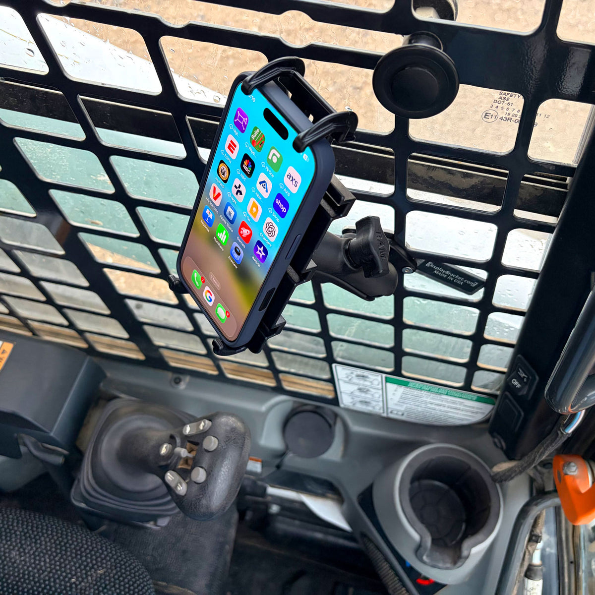 A black smartphone mount with best phone phone attached, mounted on a cab window inside a Bobcat cab.